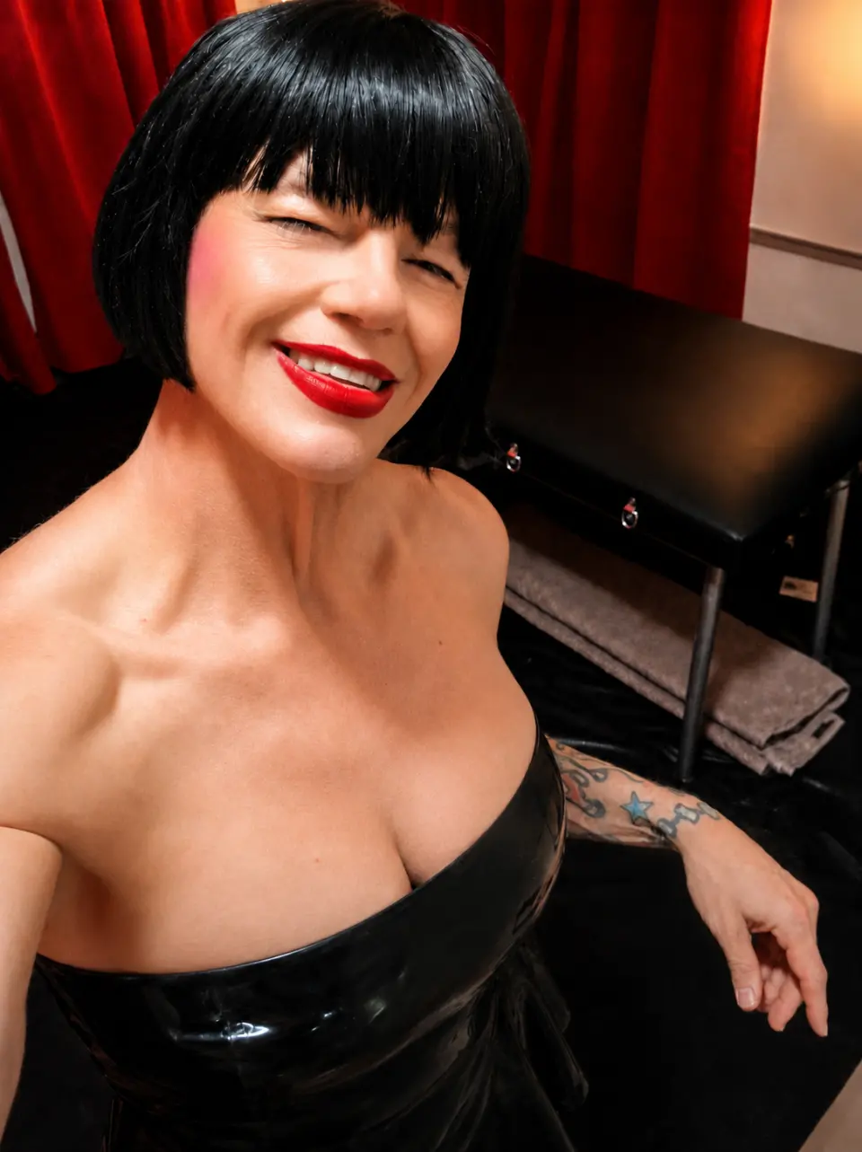 TS Mistress Mia smiling in glossy black latex in her North Dallas dungeon